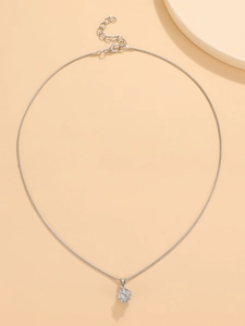 Detail of silver snake chain necklace with cubic zirconia cube pendant on beige surface