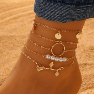 Detail of five-layer gold anklet set with pearls and rose charms on beach skin