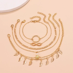 5-piece gold layered anklet set with infinity charms and pearls on pink backdrop