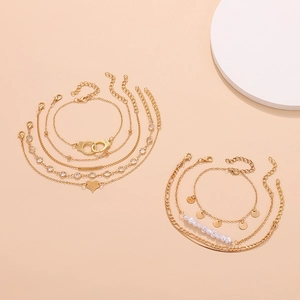 Detail of layered gold anklet set with handcuffs, heart charms and faux pearls