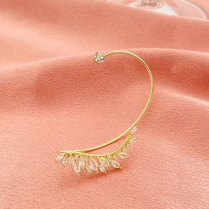Close-up of golden leaf ear cuff with sparkling zircon stones on pink silk fabric