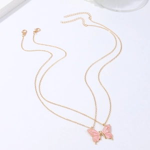 Detail van twee gouden vlinder vriendschapshangers met roze emaille op witte achtergrond