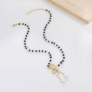 Dettaglio della collana con fiocco dorato, perline a cuore nere e ciondoli di perle