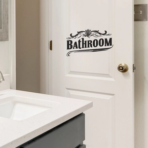 Sticker mural élégant noir pour salle de bain avec volutes sur une porte en bois blanc