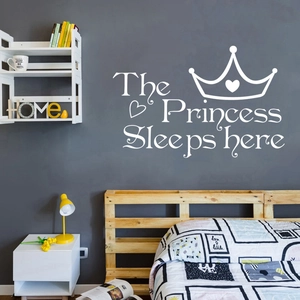Détail du sticker mural blanc The Princess Sleeps Here avec couronne sur un mur gris foncé