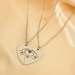 Detailed macro view of interlocking heart pendants with hand gestures and letter engraving