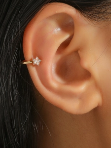 Detalle de ear cuff floral dorado con circonitas blancas puesto en la hélice de la oreja