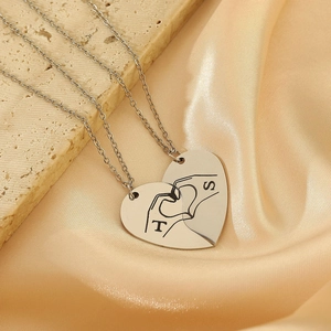 Macro detail of silver heart puzzle necklaces with engraved letters and hand sign