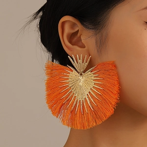 Close-up of bohemian orange tassel fan earrings on a model with gold metal detailing