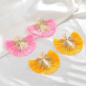 Detail of bohemian fan-shaped tassel earrings in pink and yellow colors on white silk
