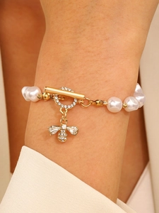 Detailed close-up of a pearl bracelet with a golden bee pendant and T-bar toggle clasp