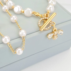 Macro shot of gold OT clasp and diamond bee pendant on baroque pearl bracelet