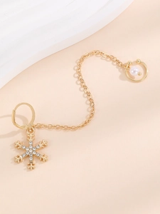 Detail of golden snowflake earring with rhinestone pendant, chain, and pearl cuff