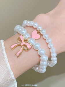 Close-up of double-layer pearl bracelet with pink enamel bow and heart pendants
