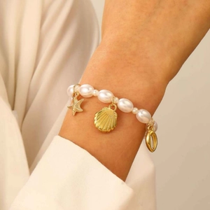 Detail of baroque pearl bracelet with gold starfish and seashell charms on wrist