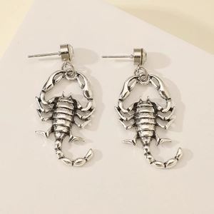 Close-up of vintage silver scorpion earrings with crystal studs on geometric surface