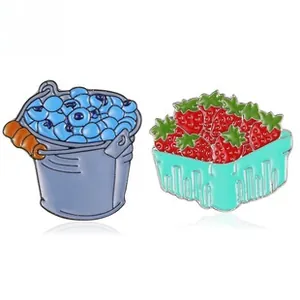 Detalle de pines de esmalte de colores con un cubo de arándanos y una cesta de fresas