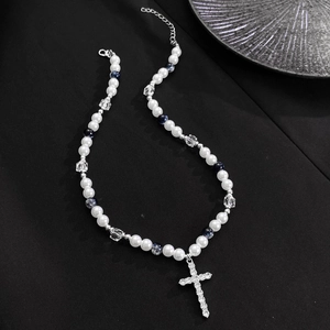 Macro detail of pearl necklace with rhinestone cross pendant on black background