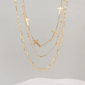 Detailed close-up of a three-layer gold necklace with cross pendants and paperclip chains