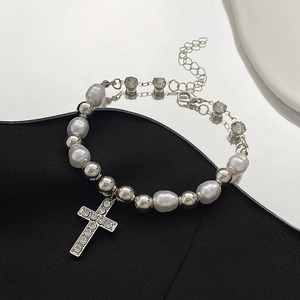 Detail of beaded bracelet featuring white pearls and rhinestone cross pendant on dark surface