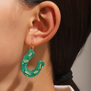 Primer plano de pendientes de herradura de resina verde con cristales en el modelo de oreja