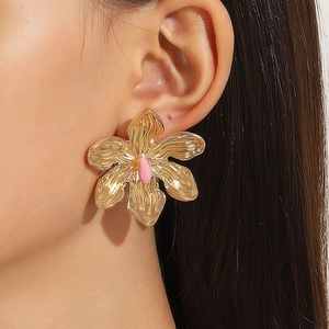 Detail of oversized gold flower earring with pink center on a model's ear