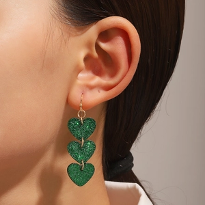 Primer plano de pendientes de triple corazón con purpurina verde usados en oreja