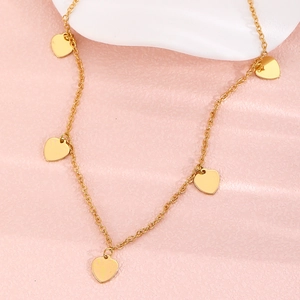 Elegante goldene Doppelhalskette mit fünf polierten Herzanhängern auf rosa strukturiertem Grund