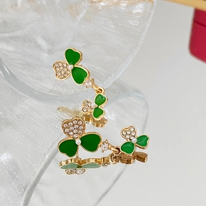 Detalle de pendientes de trébol con esmalte verde, bordes dorados, perlas y cristales