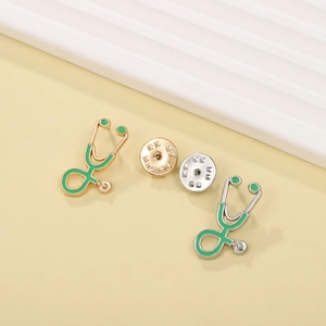 Detail of gold and silver stethoscope brooches with green enamel on a light background