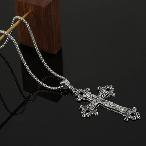 Macro detail of gothic antique silver cross pendant with floral vine relief on a dark box chain