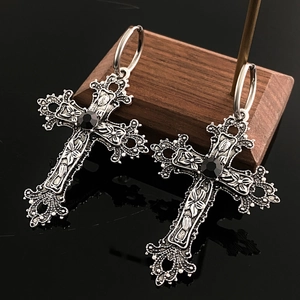 Macro shot of gothic cross earrings featuring floral relief and a black gemstone