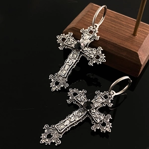 Macro view of gothic silver cross earring with black gemstone on reflective surface