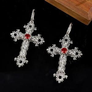 Gothic silver cross earrings with vine relief and red gemstone on black surface