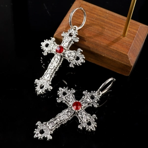 Macro detail of gothic silver cross earrings with ornate flower vine and red center gemstone
