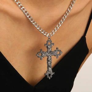 Macro detail of gothic silver cross pendant with baroque floral patterns and curb chain