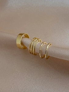 Close-up of four-piece gold ear cuff set hanging on elegant champagne silk fabric