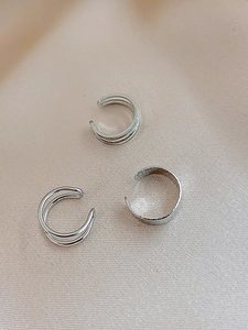 Macro shot of silver metal ear cuffs set on light beige satin background showing wave texture