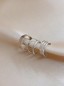 Close-up of three silver C-shaped ear clips on elegant champagne silk fabric