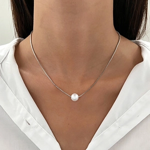 Close-up of a minimalist single pearl pendant necklace on a silver-white chain worn by a model