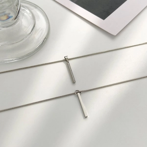 Detail of silver spiral and square column pendant necklaces on a minimalist white backdrop