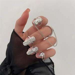 Detalle de set de anillos de metal líquido plateado con circonita de corazón y cadena en mano
