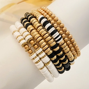 Detailed view of elastic Heishi bracelets with black, white clay beads and gold accents