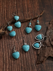 Close-up of bohemian turquoise heart earrings with silver accents on a wooden texture