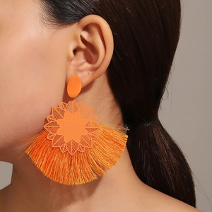 Detalle de pendientes grandes con borlas naranjas y placa floral usados por el modelo