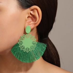 Primer plano de pendientes bohemios verde esmeralda con borlas y detalle de flores