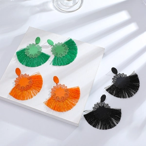 Detalle de pendientes boho con borlas en verde, naranja y negro con textura de tela