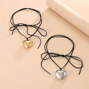 Detailed view of polished gold and silver heart pendants on black cord bow necklaces