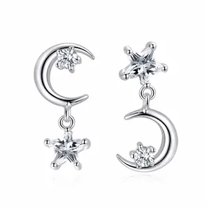 Détail de boucles d'oreilles asymétriques argentées avec charms lune et étoile en zircon