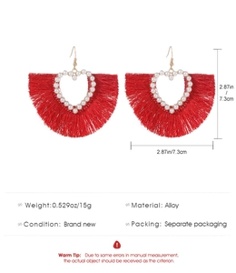 Detail showing red fan-shaped tassel earrings with heart cut-out and pearls